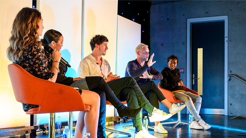Group of five people sat on a stage talking to an audience